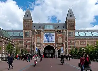 Photo of a largely symmetrical building with two square towers and with a tunnel for a street through the center